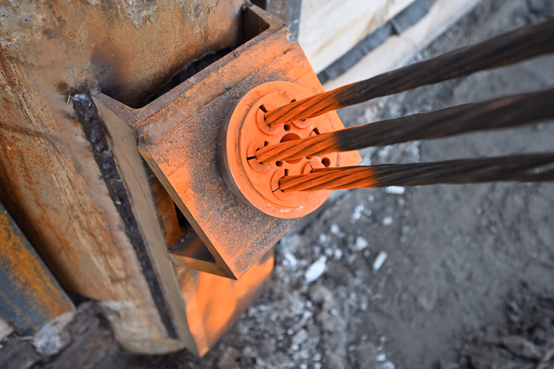 Close-up of steel cables anchored to a rusty metal structure with a circular orange mounting plate.