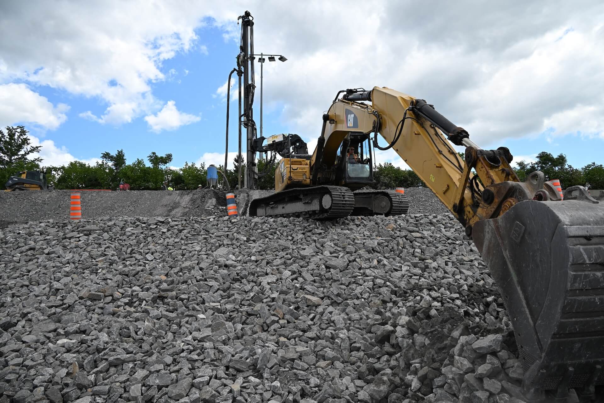 Yellow CAT excavator on a gravel slope at a construction site under a partly cloudy sky.